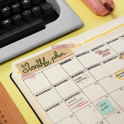 Una agenda abierta mostrando un plan mensual con anotaciones manuscritas, destacando un "Monthly plan" en una pestaña de papel y fechas importantes.