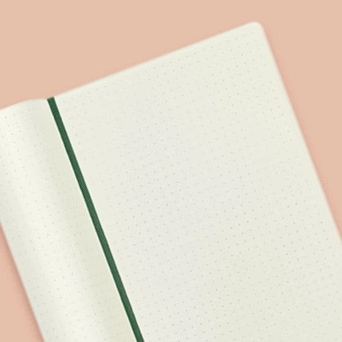libreta abierta mostrando páginas punteadas de color crema con una cinta separadora verde oscuro.