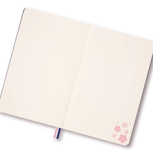 Una libreta abierta con páginas en blanco y un pequeño diseño de flores de cerezo rosas en la esquina inferior derecha.